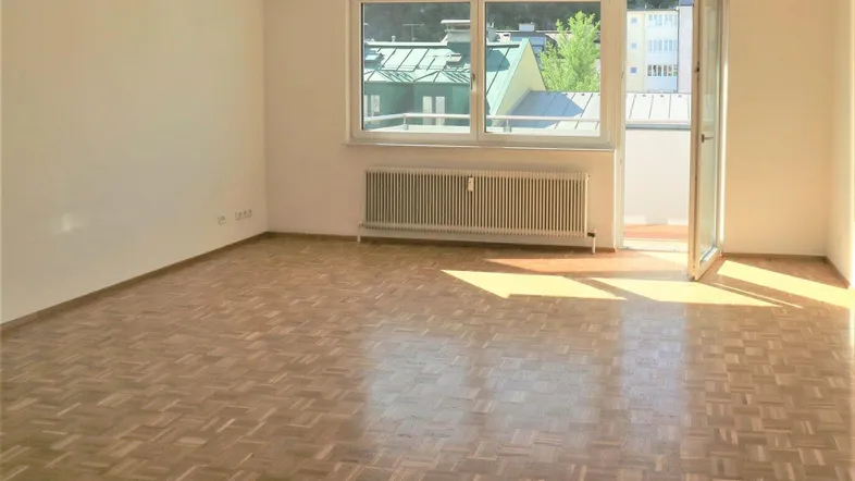 Helles Zimmer mit Parkettboden, großem Fenster und Zugang zu einem Balkon.