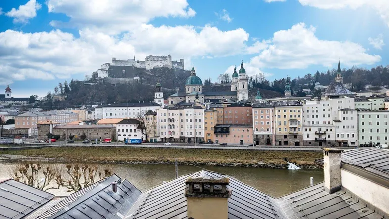 Panoramablick über die Stadt Salzburg mit Festung Hohensalzburg und Fluss im Vordergrund.