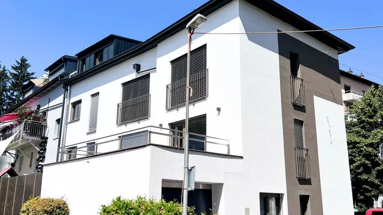 Moderne Architektur mit weißer und grauer Fassade, Balkonen und Rollläden unter blauem Himmel.