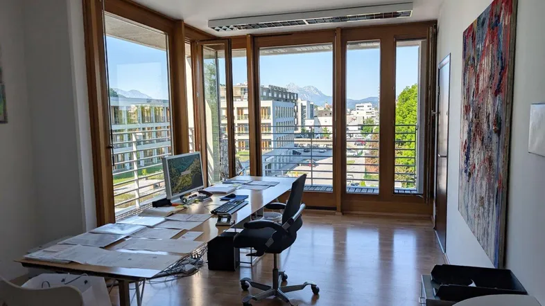 Helles Büro mit großen Fenstern, Holzboden und einem weiten Blick auf die Stadt und Berge.