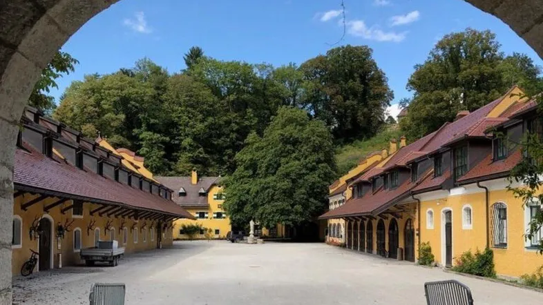 Historischer Innenhof mit gelben Gebäuden und grüner Umgebung unter blauem Himmel.