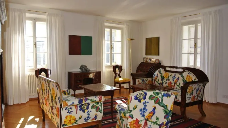 Helles Wohnzimmer mit farbenfrohen Sofas, Parkettboden und klassischen Holzmöbeln, durchflutet von natürlichem Licht.