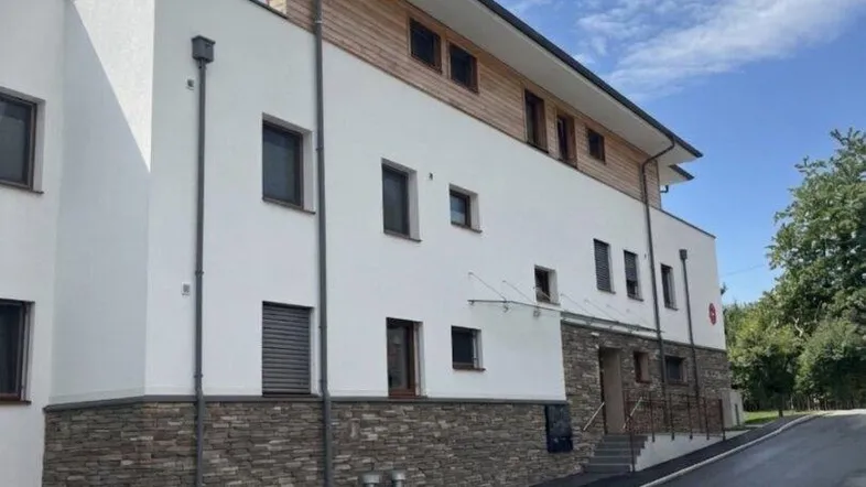 Moderne Architektur mit weißer Fassade, Holzverkleidung und Steinsockel unter blauem Himmel.