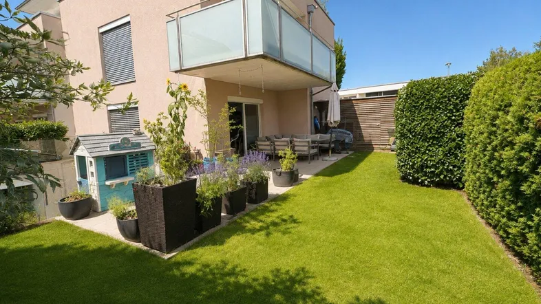 Gepflegter Gartenbereich mit Rasenfläche und einer möblierten Terrasse am modernen Wohnhaus.