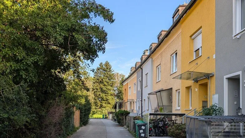 Reihenhäuser in einer ruhigen Wohnstraße mit viel Grün und blauem Himmel.