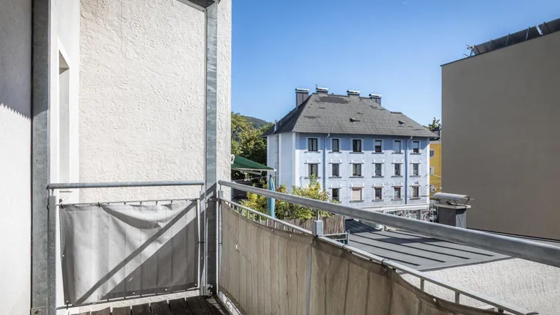 Balkon mit Holzboden und Blick auf die umliegenden Gebäude und grüne Hügel.