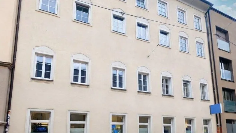 Ansicht der hellbeigen Fassade eines mehrstöckigen Gebäudes mit vielen Fenstern und einem blauen Himmel.
