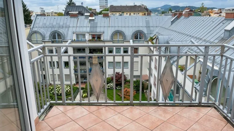 Geräumiger Balkon mit Fliesenboden und Blick auf die umliegenden Gebäude und einen begrünten Innenhof.