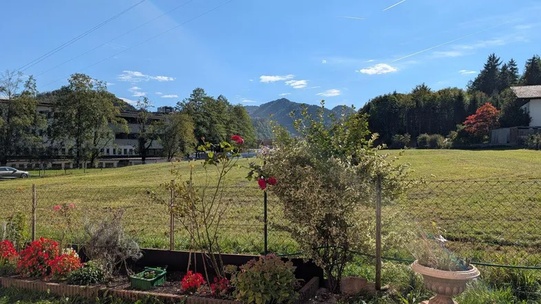 Gepflegter Gartenbereich mit Blumenbeet, Rasenfläche und Bergblick im Hintergrund.