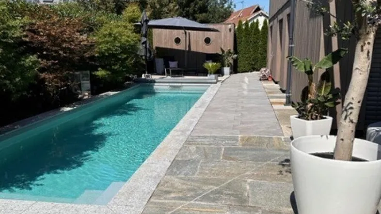 Außenbereich mit langem Swimmingpool, gepflastertem Weg und gepflegtem Rasen neben dem modernen Gebäude.