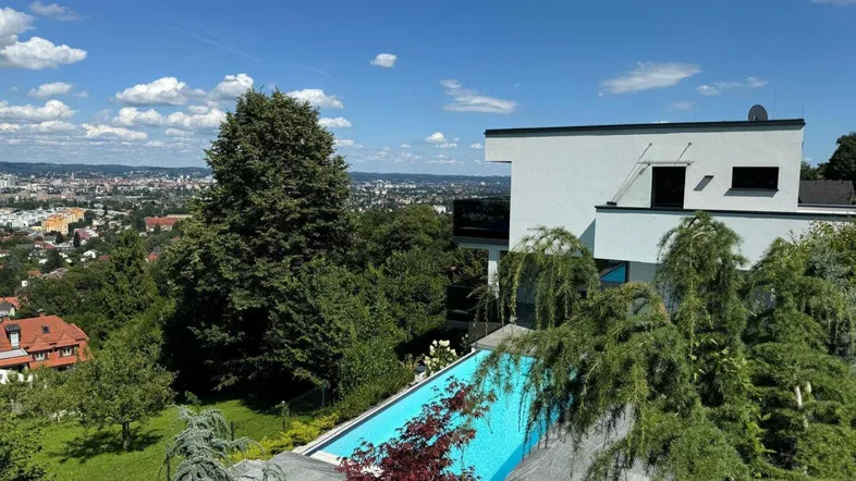 Moderne Villa mit Infinity-Pool und weitem Blick über die Stadtlandschaft unter blauem Himmel.
