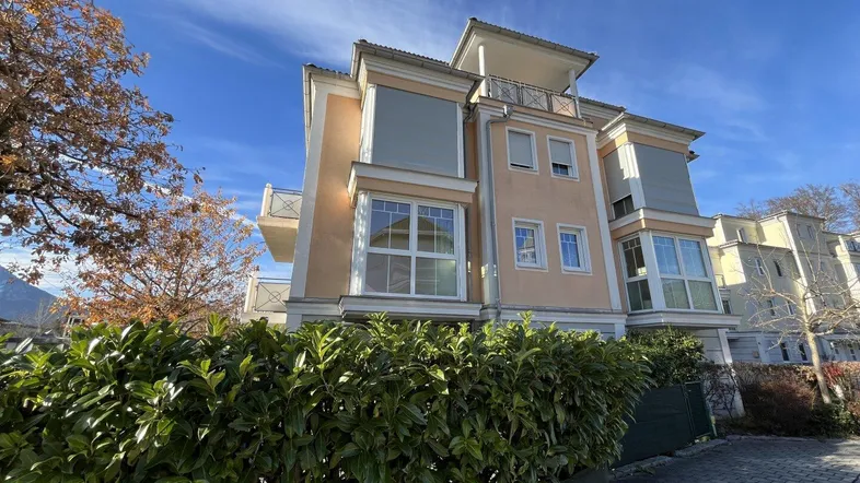 Modernes Mehrfamilienhaus mit beiger Fassade, großen Fenstern und gepflegter Hecke im Vordergrund.