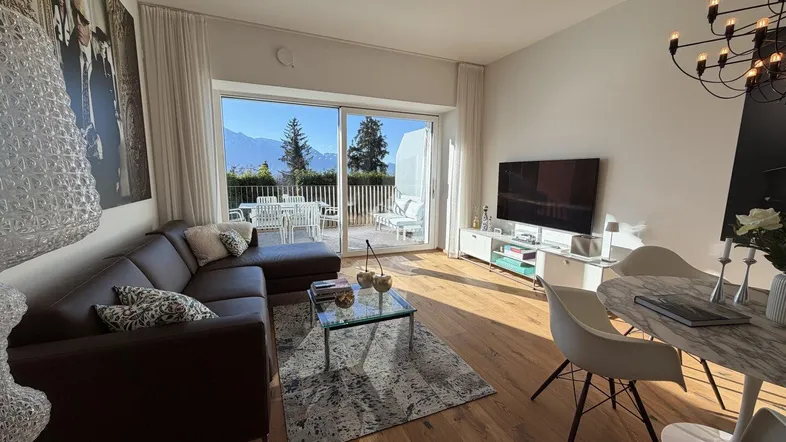 Helles Wohn- und Esszimmer mit Holzboden, gemütlichem Sofa und Zugang zur Terrasse mit Bergblick.