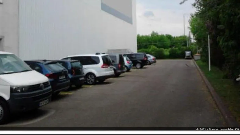 Außenansicht eines modernen Gebäudes mit großem Parkplatz und geparkten Fahrzeugen davor.