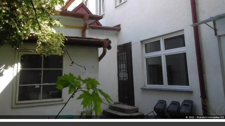 Außenansicht eines Gebäudes mit weißer Fassade, Fenstern und einem Eingangsbereich, umgeben von Bäumen.