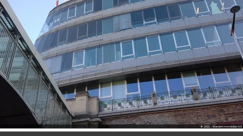 Modernes Bürogebäude mit Glasfassade und einem Übergangssteg im Vordergrund unter blauem Himmel.