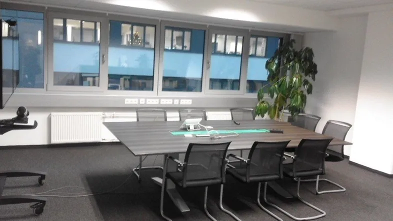 Moderner Konferenzraum mit großem Tisch, bequemen Stühlen und Blick auf umliegende Gebäude.