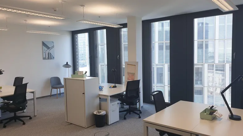 Helles und modernes Büro mit mehreren Arbeitsplätzen und großen Fenstern mit Stadtblick.