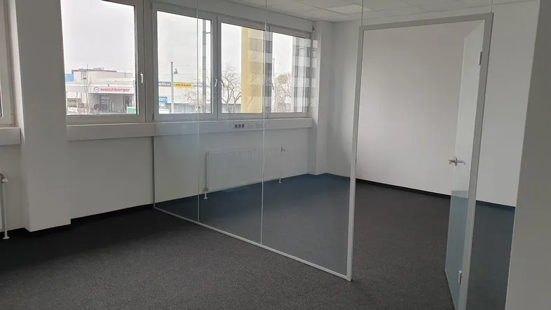 Helles Büro mit Teppichboden und großen Fenstern, die einen Blick auf die Umgebung bieten.