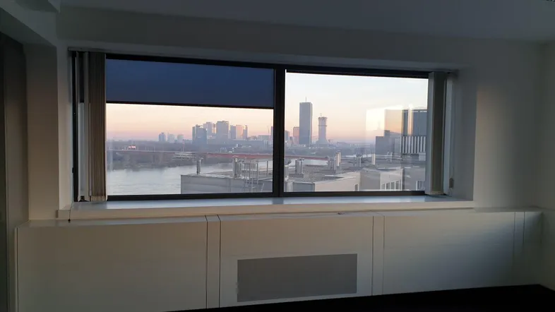 Großes Fenster mit Panoramablick auf die Stadt bei Sonnenuntergang, darunter eine lange weiße Ablage.