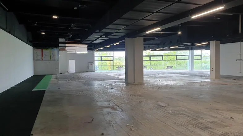 Großer, offener Gewerberaum mit hohen Decken, Betonboden und großen Fenstern, die viel Tageslicht hereinlassen.