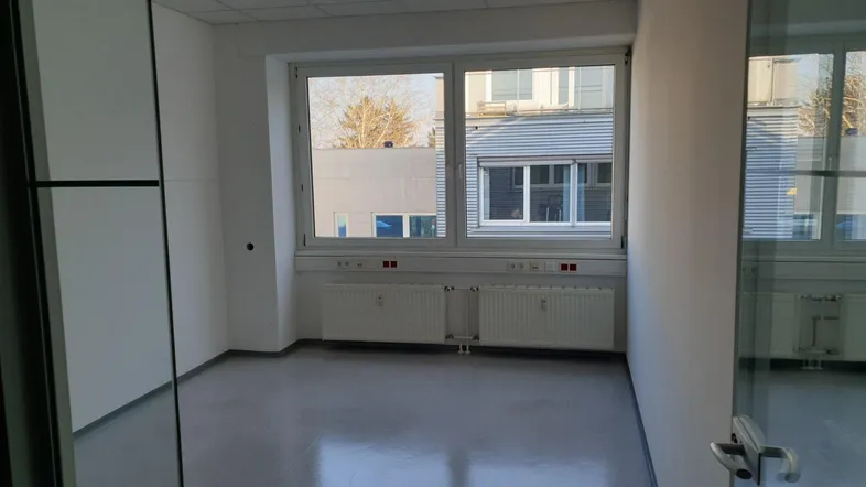 Heller Büroraum mit großen Fenstern, die viel Tageslicht hereinlassen und Blick auf umliegende Gebäude bieten.