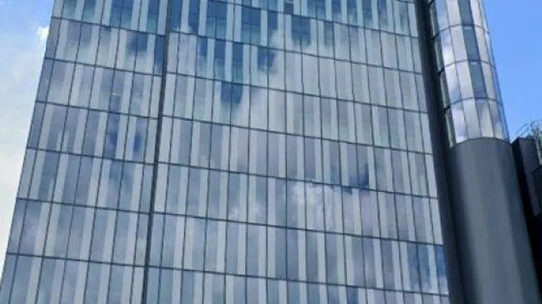 Modernes Hochhaus mit Glasfassade und vielen Fenstern unter blauem Himmel, umgeben von Autos.