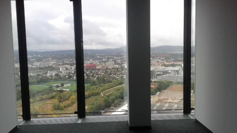 Leerer Büroraum mit großen Fenstern und weitem Blick über die Stadt und grüne Landschaften.