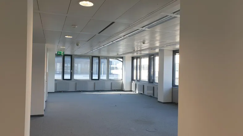 Geräumiges, leeres Büro mit großen Fenstern, die viel Tageslicht hereinlassen und einen weiten Blick bieten.