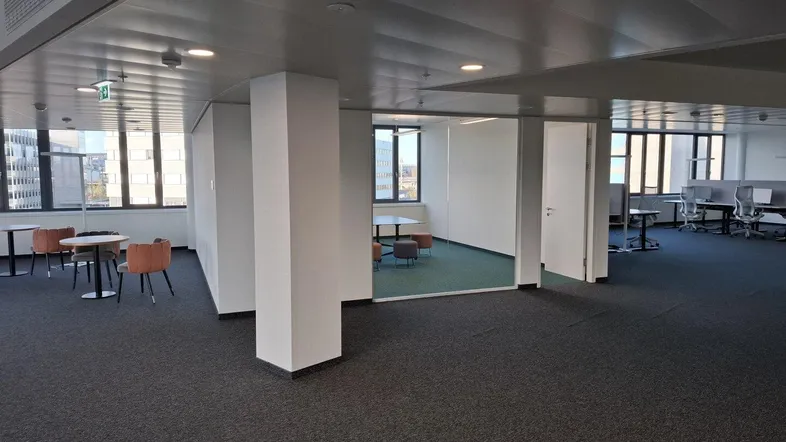 Großes, offenes Büro mit Teppichboden, großen Fenstern und modernen Sitzbereichen für Besprechungen.