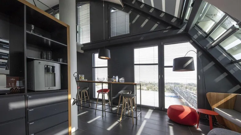 Moderner Pausenbereich mit Bar, dunklen Fliesen und großer Fensterfront, die einen weiten Blick bietet.
