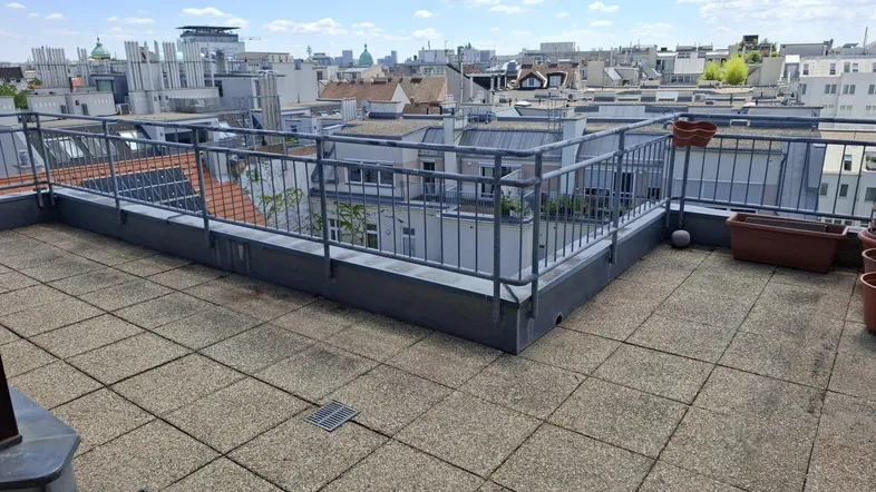 Geräumige Dachterrasse mit Stadtblick und Metallgeländer, ideal für Entspannung im Freien.