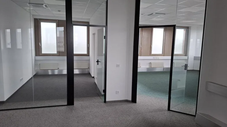 Heller Büroraum mit Glaswänden und Teppichboden, bietet viel natürliches Licht und moderne Trennwände.