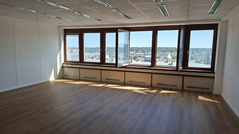 Geräumiges Büro mit großen Fenstern, Laminatboden und weitem Blick über die Stadt.