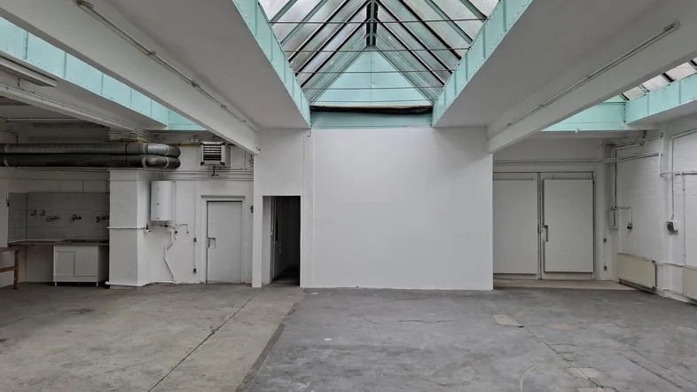 Großer, leerer Industrieraum mit Betonboden, weißen Wänden und einem beeindruckenden Glasdach für viel Tageslicht.