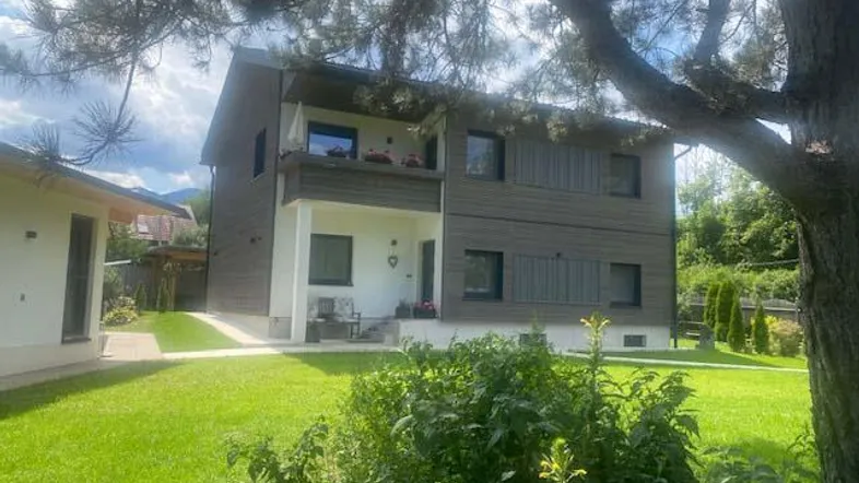 Modernes Wohnhaus mit Holzfassade, kleinem Vorgarten und Balkon in grüner Umgebung.
