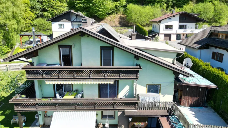 Mehrstöckiges Haus mit mehreren Balkonen und einem gepflegten Gartenbereich in grüner Umgebung.