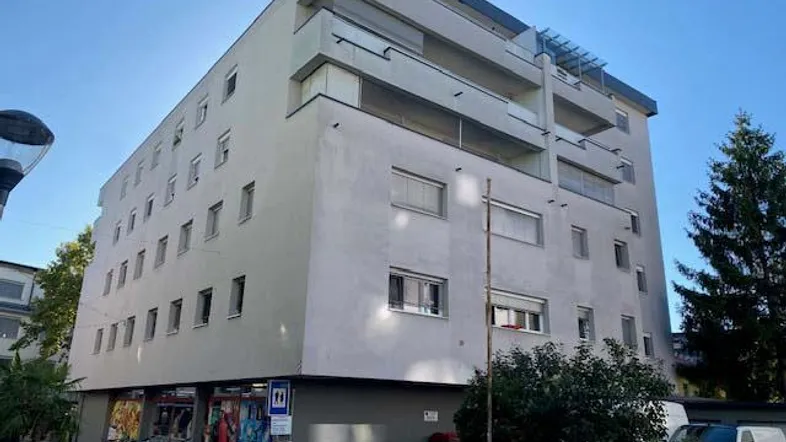 Modernes Mehrfamilienhaus mit Geschäften im Erdgeschoss und Balkonen in den oberen Etagen.