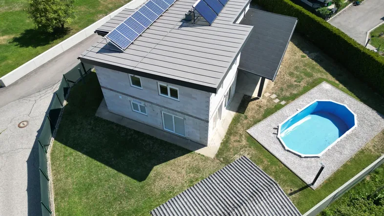 Luftaufnahme des Neubaus mit Solarmodulen auf dem Dach und einem Pool im Garten, umgeben von Grünflächen.