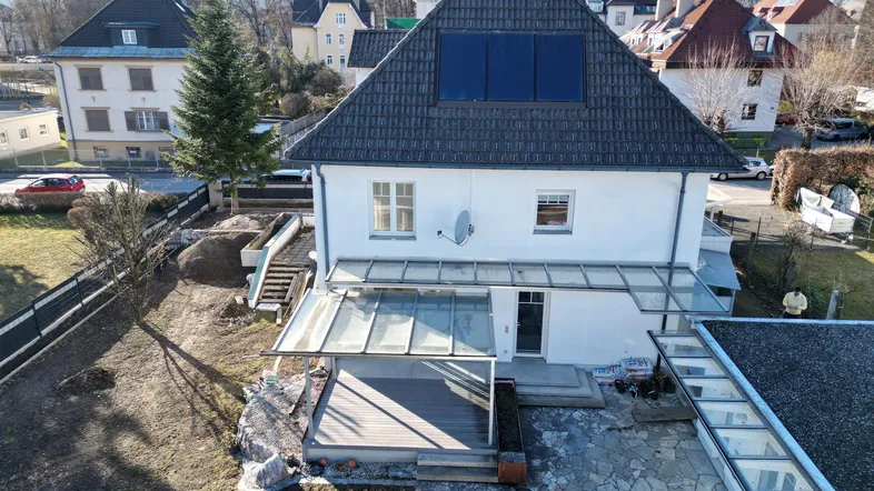 Luftaufnahme des Hauses mit Dach, Solarpaneelen, Terrasse und Gartenbereich in einer Wohngegend.
