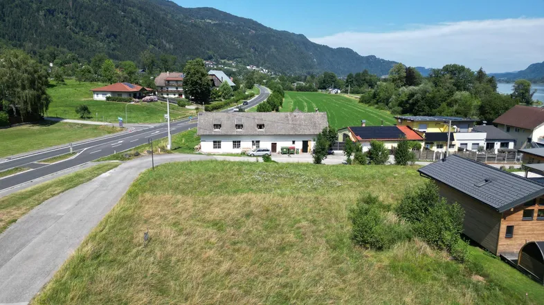 Luftaufnahme eines Grundstücks mit Haus, Straße, grünen Feldern und Bergen im Hintergrund.