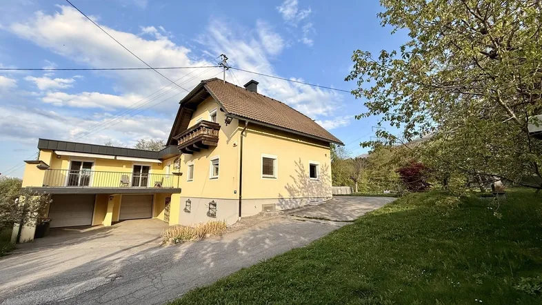 Gelbes Wohnhaus mit Satteldach, Balkon und integrierter Doppelgarage in ländlicher Umgebung.