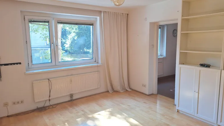 Helles Wohnzimmer mit Parkettboden, großem Fenster und Blick ins Grüne.