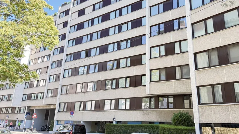 Mehrstöckiges Wohngebäude mit vielen Fenstern und gepflegter Fassade an einer städtischen Straße.