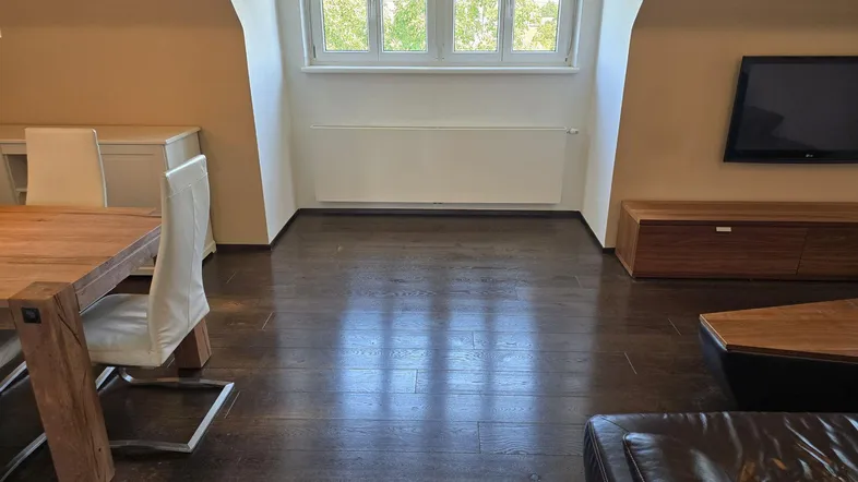 Helles Dachgeschoss-Wohnzimmer mit Holzboden, großem Fenster und Blick ins Grüne.