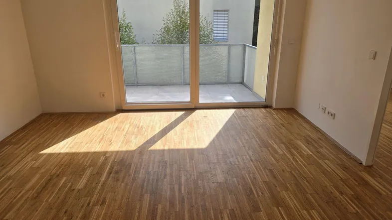 Helles Wohnzimmer mit Parkettboden und großem Fenster, das Zugang zum Balkon bietet.