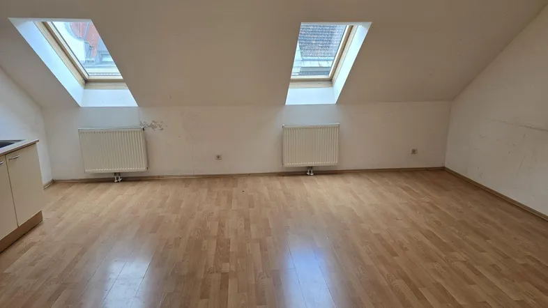 Heller Dachgeschossraum mit Laminatboden, schrägen Wänden und zwei Dachfenstern, ideal als Wohnbereich.