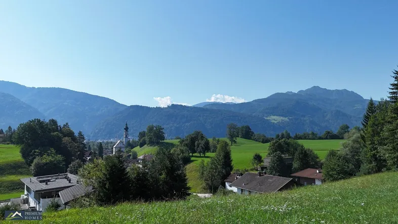 Landschaftliche Ansicht mit grünen Hügeln, Häusern und einer Kirche im Tal, umgeben von Bergen.