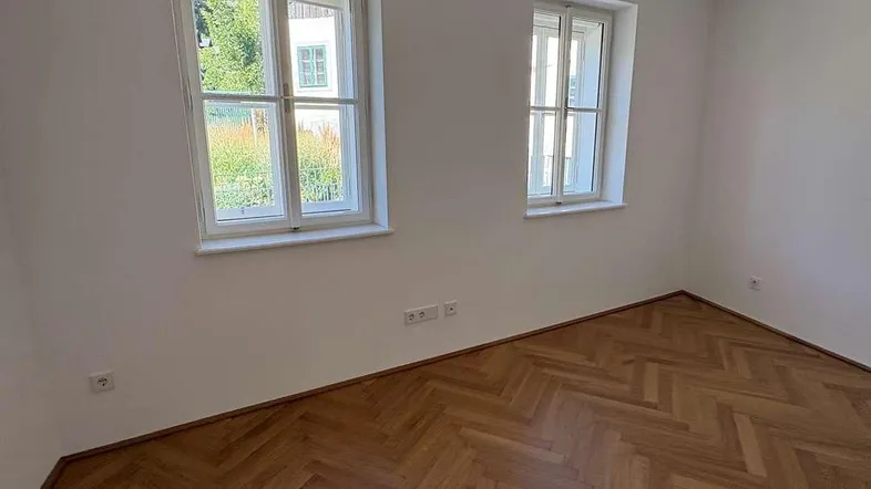 Heller Raum mit Fischgrätparkettboden und zwei Fenstern, bereit zur individuellen Gestaltung.