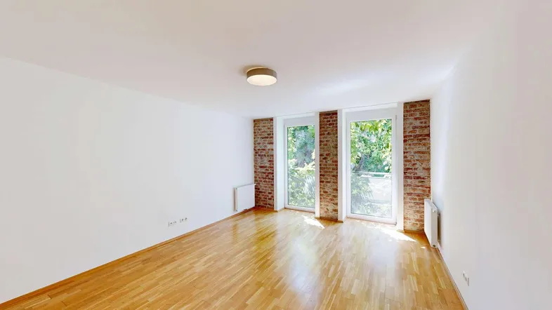 Helles Zimmer mit Holzboden, weißen Wänden und großen Fenstern mit Blick ins Grüne.